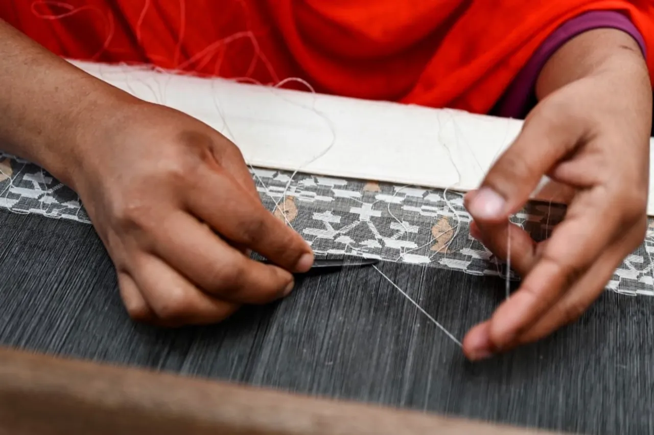 A weaver’s hands working a motif into fine cloth on the loom